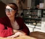 Woman in a wheelchair enjoying a sunny day at a café, wearing eyeglasses and a red jacket.